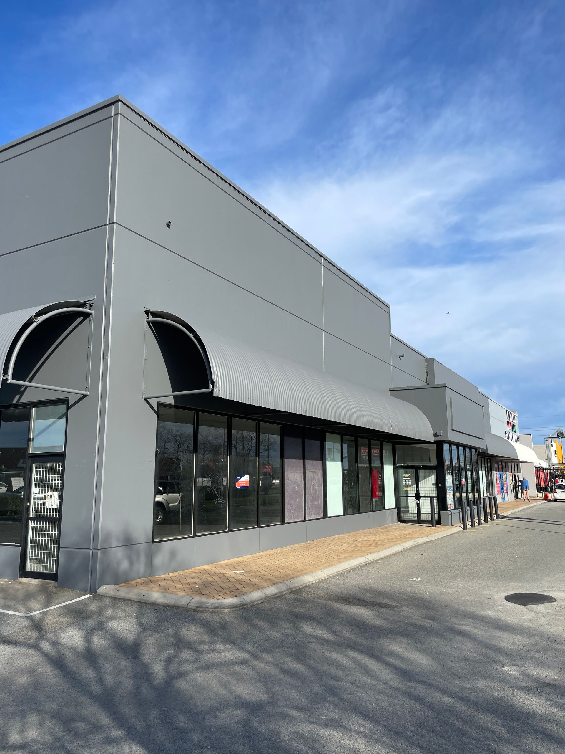 Gray storefront building with black awnings, large windows, and a sunny sky.