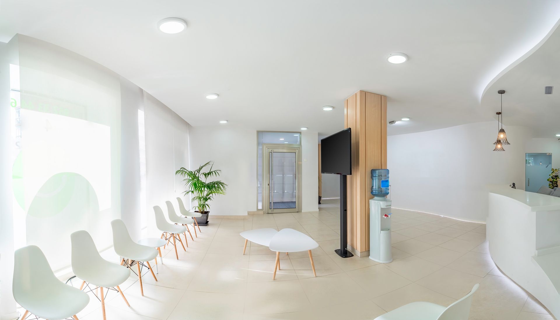 A reception and waiting room in a clinic with a desk, chairs, and plants, after commercial fitout.