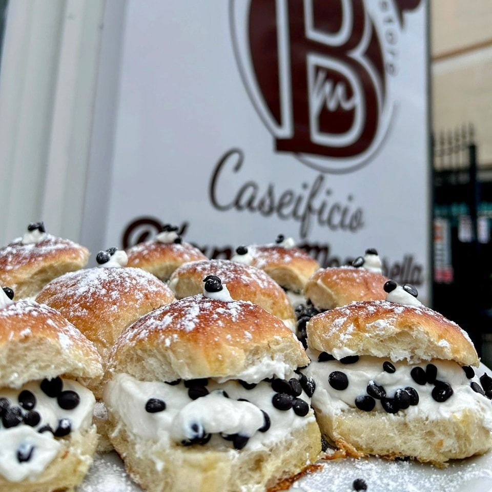 Pasticcini ripieni di crema e gocce di cioccolato, spolverati con zucchero a velo, davanti all'insegna di un bar.