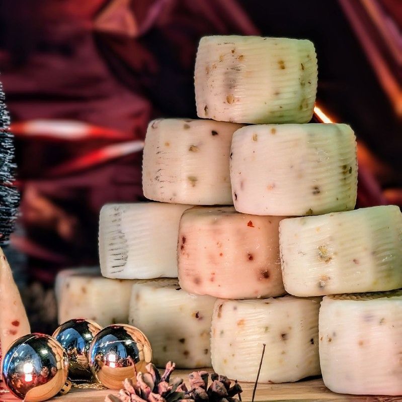 Pila di forme di formaggio, punteggiate di inclusioni, su una superficie di legno con decorazioni natalizie e uno sfondo festivo.