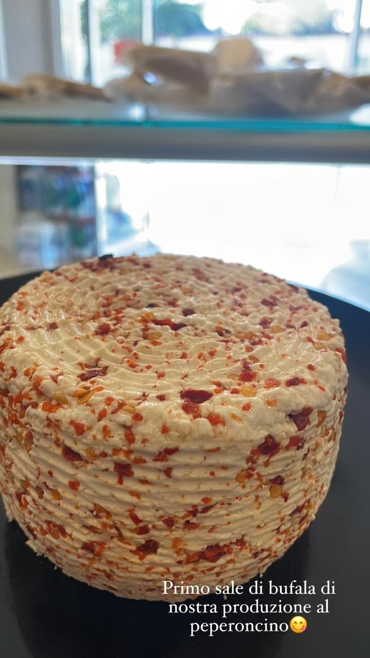 Formaggio rotondo di latte di bufala con fiocchi di peperoncino rosso, presentato su un piatto nero.