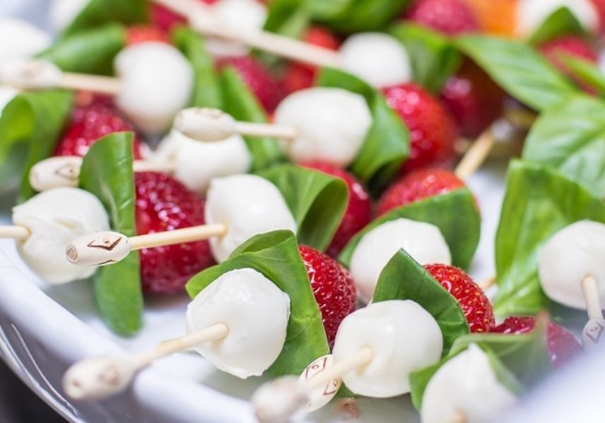 Spiedini di fragole, mozzarella e basilico su un piatto bianco.