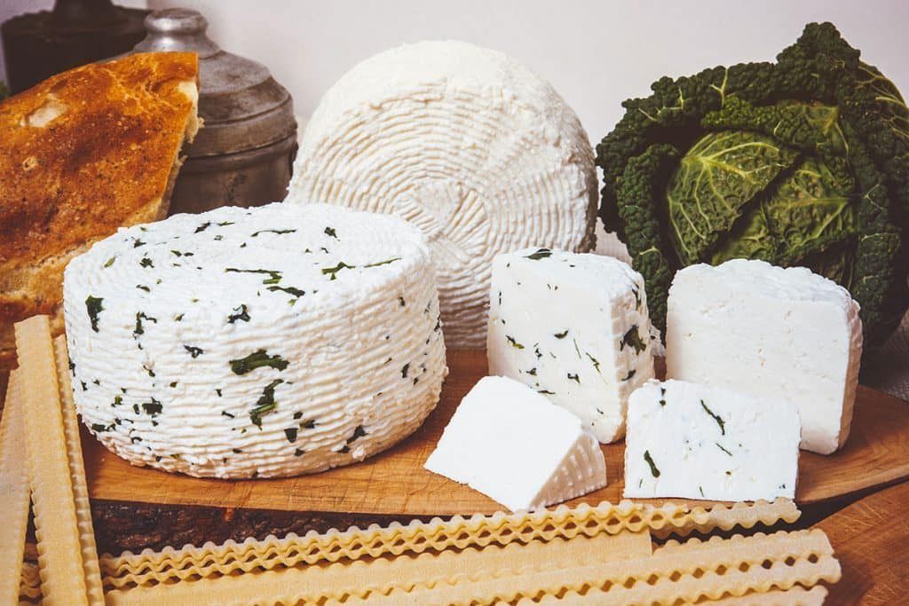 Assortimento di formaggi con erbe aromatiche, una testa di cavolo e pasta su una superficie di legno.