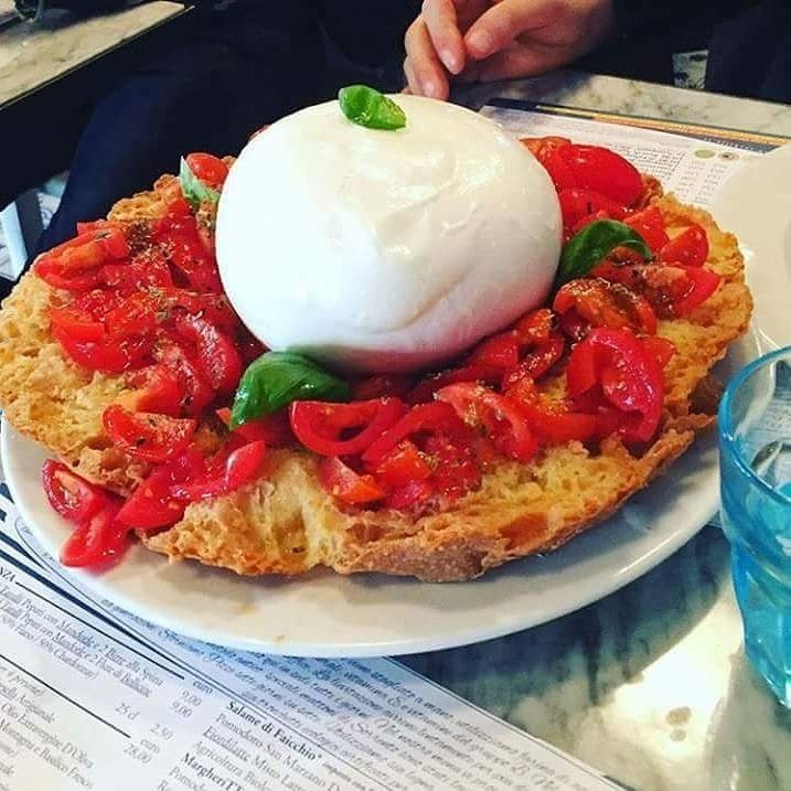 Pallina di burrata su una grande base di pane con pomodori a cubetti e basilico su un piatto.