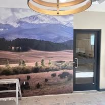 A wall mural of a snowy mountain range above a grassy field with grazing buffalo next to a glass-paneled doorway.