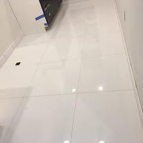 Glossy white floor tiles with a dark cabinet in the corner of a room.