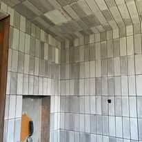A corner of a room featuring light-grey, vertically stacked rectangular wall and ceiling tiles and an unfinished doorway.