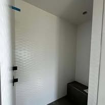 A small room with textured white walls, black door hinges, and a dark bench in the corner.