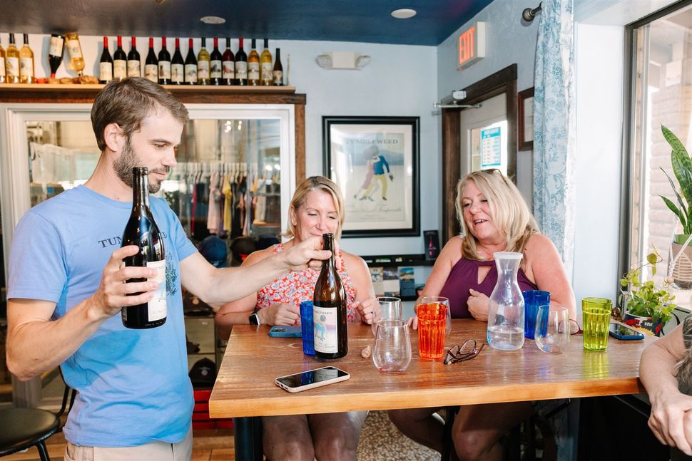 A man is holding a bottle of wine while two women sit at a table.
