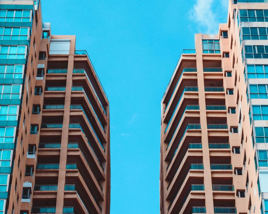 Two tall buildings with balconies against a blue sky.