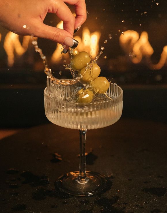 A person is pouring olives into a martini glass