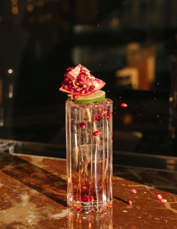 A glass of water with a slice of pomegranate on top of it.