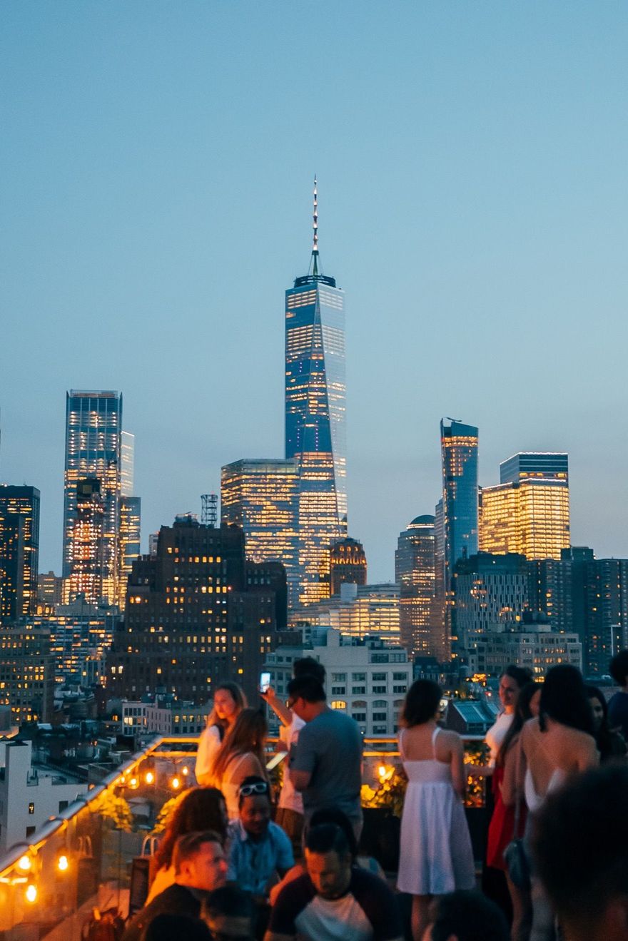 A group of people are standing on a rooftop looking at the city skyline at night.