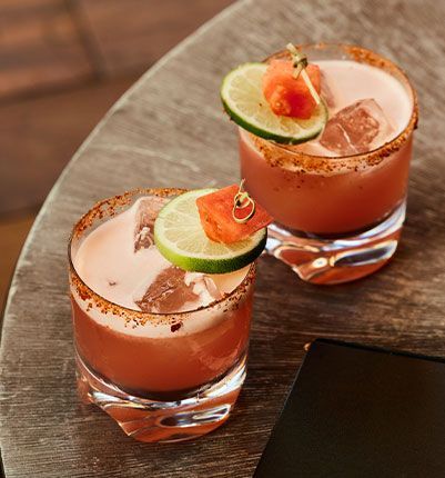 Two glasses of watermelon margarita on a wooden table.