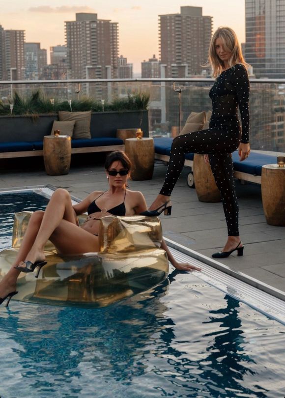 Two women in bikinis are standing next to a swimming pool.