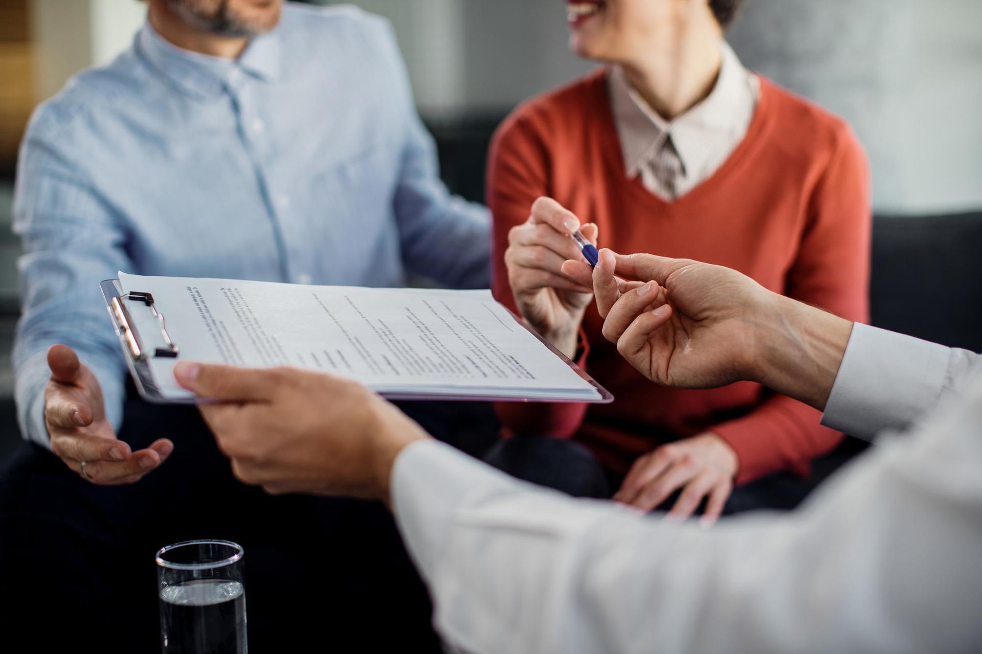 A man and a woman are sitting at a table talking to a man in a suit.