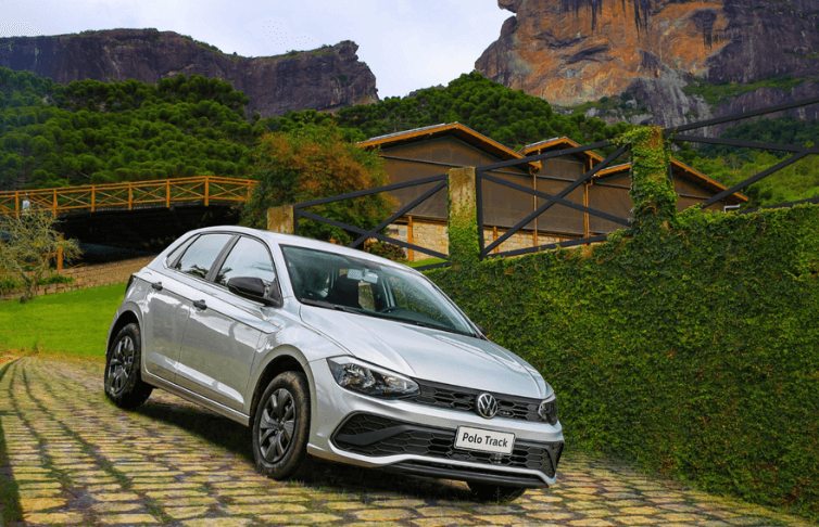 A silver car is parked on a cobblestone road in front of a mountain.