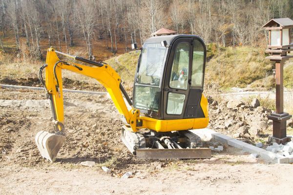 A small yellow excavator is sitting on top of a dirt field.