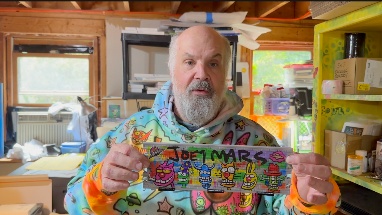 Joey Mars holds a lego wall image depicting his name in grafitti