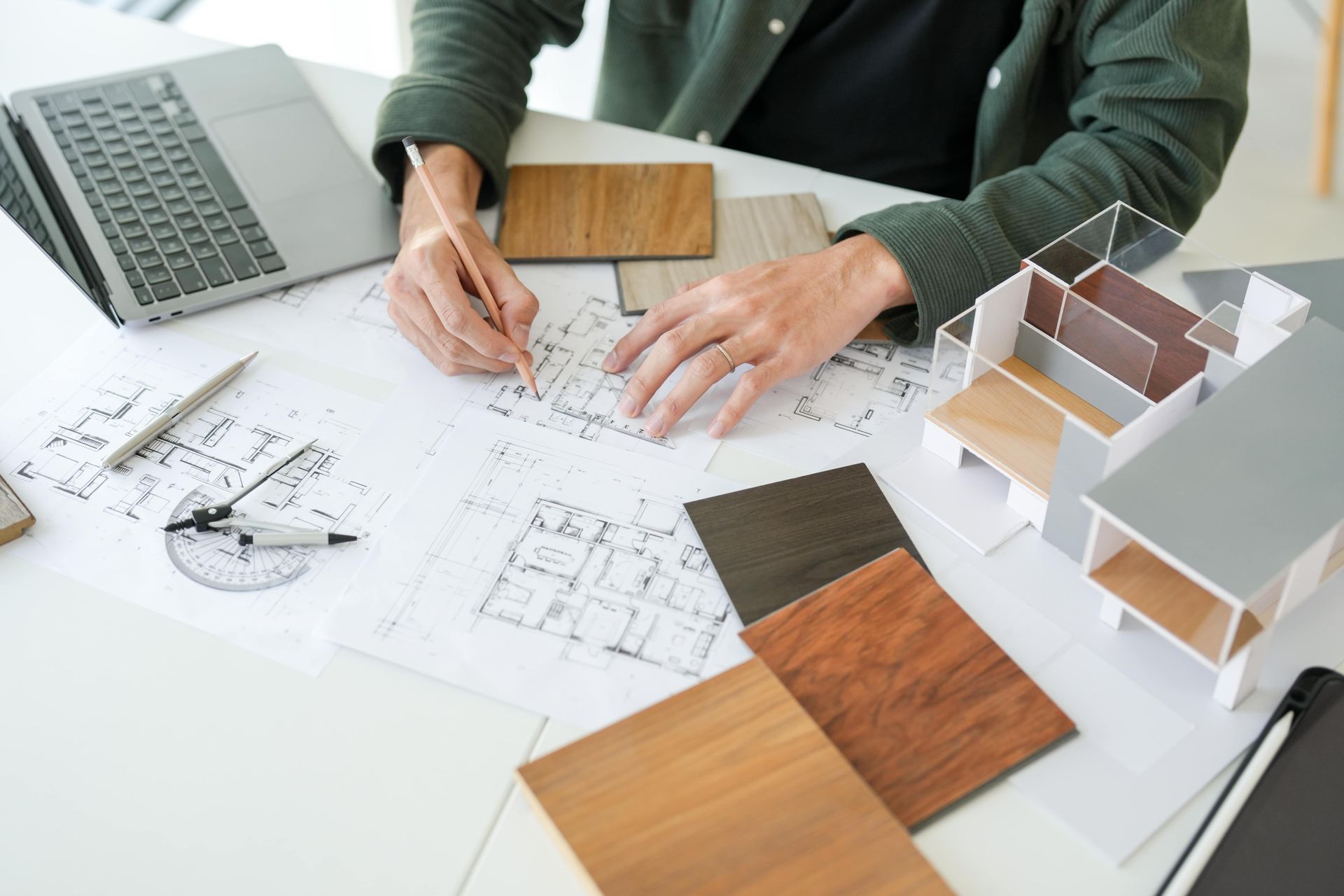 Architect reviewing floor plans and material samples at a desk with a laptop and model house.