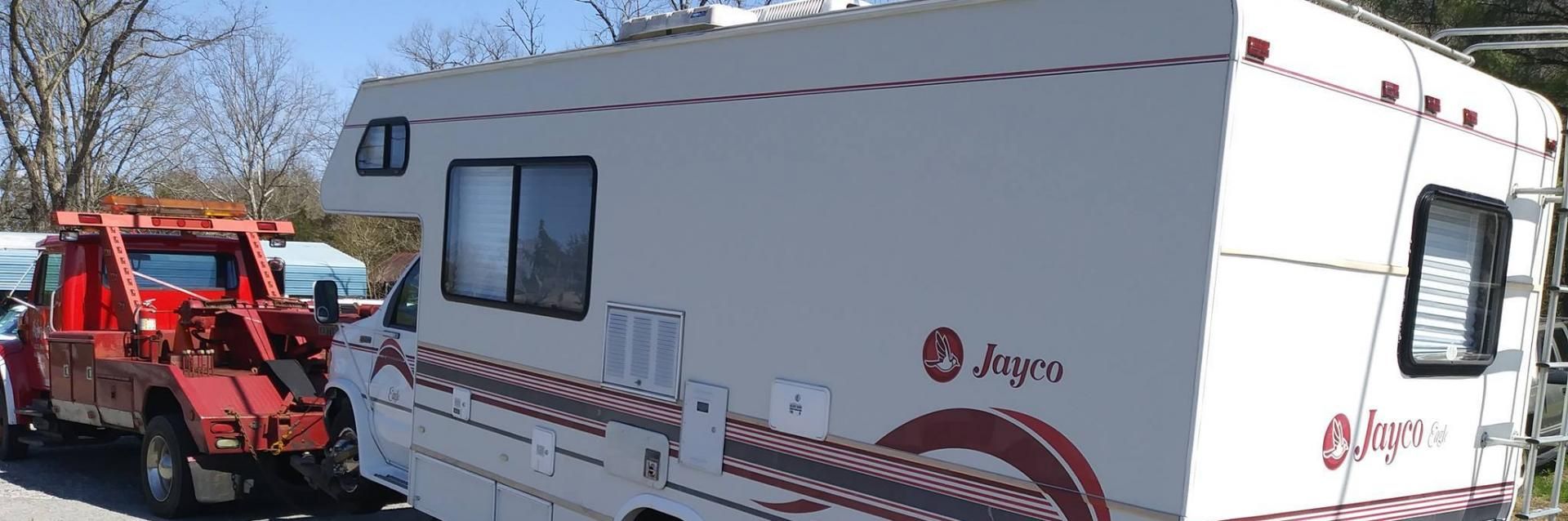 A red tow truck towing a white Argosy RV on a sunny day.