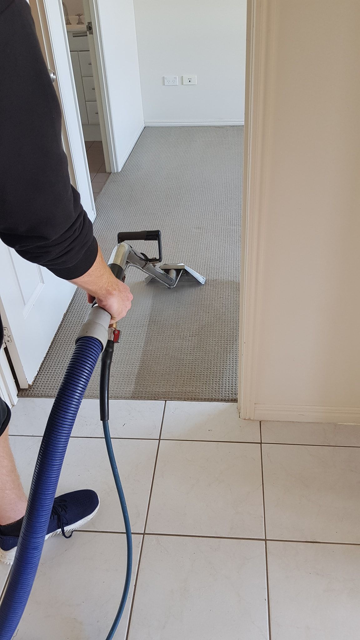 Person vacuuming a gray patterned carpet in a room with white walls and tile floors.— Dynamic Services in Limestone Creek, QLD