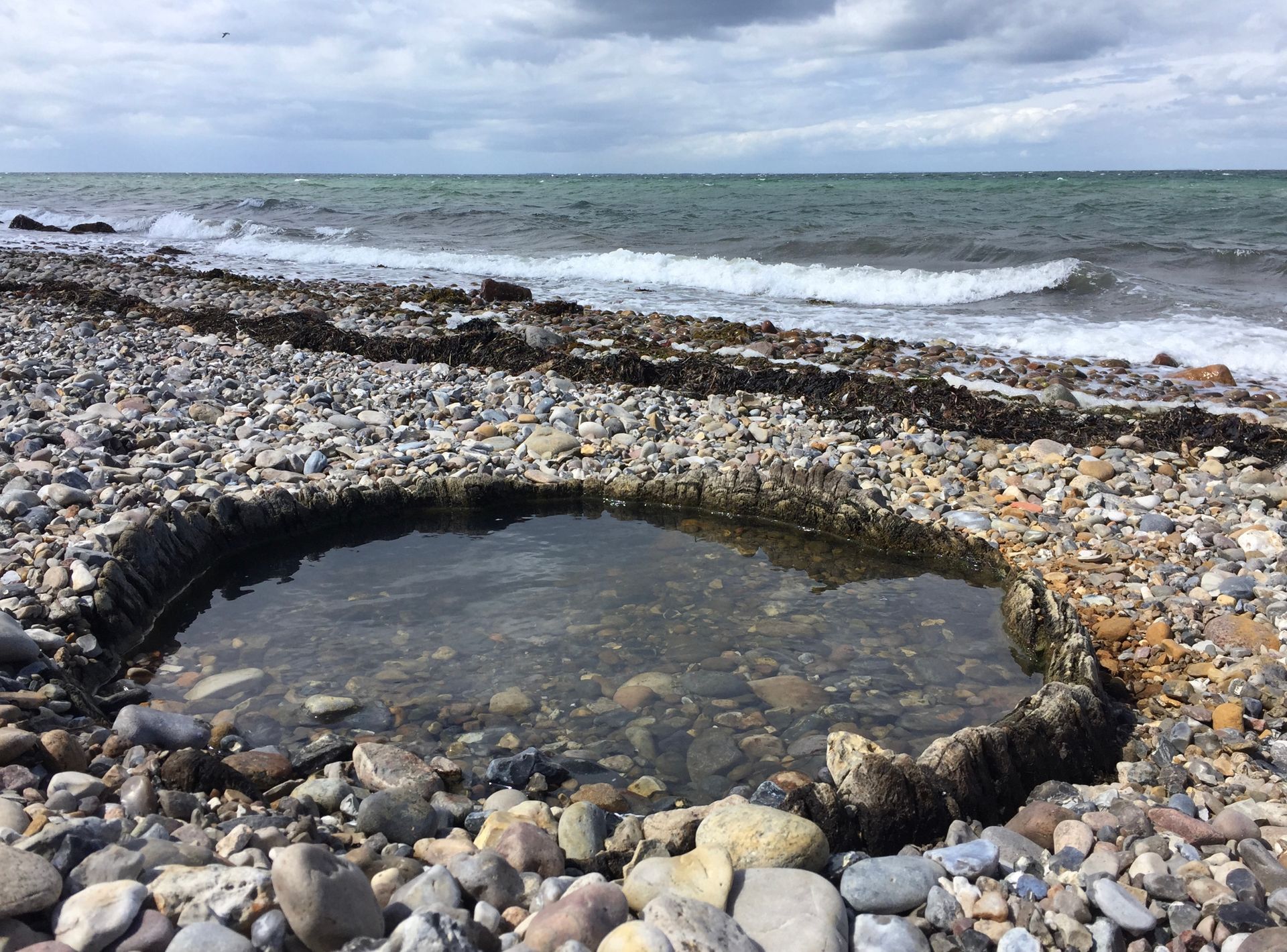 en lille pool af vand på en stenet strand ved siden af ​​havet.