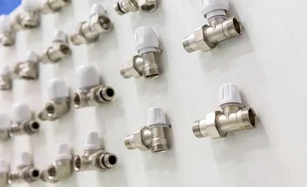 Primo piano di numerose valvole idrauliche metalliche con manopole bianche montate su una superficie bianca.