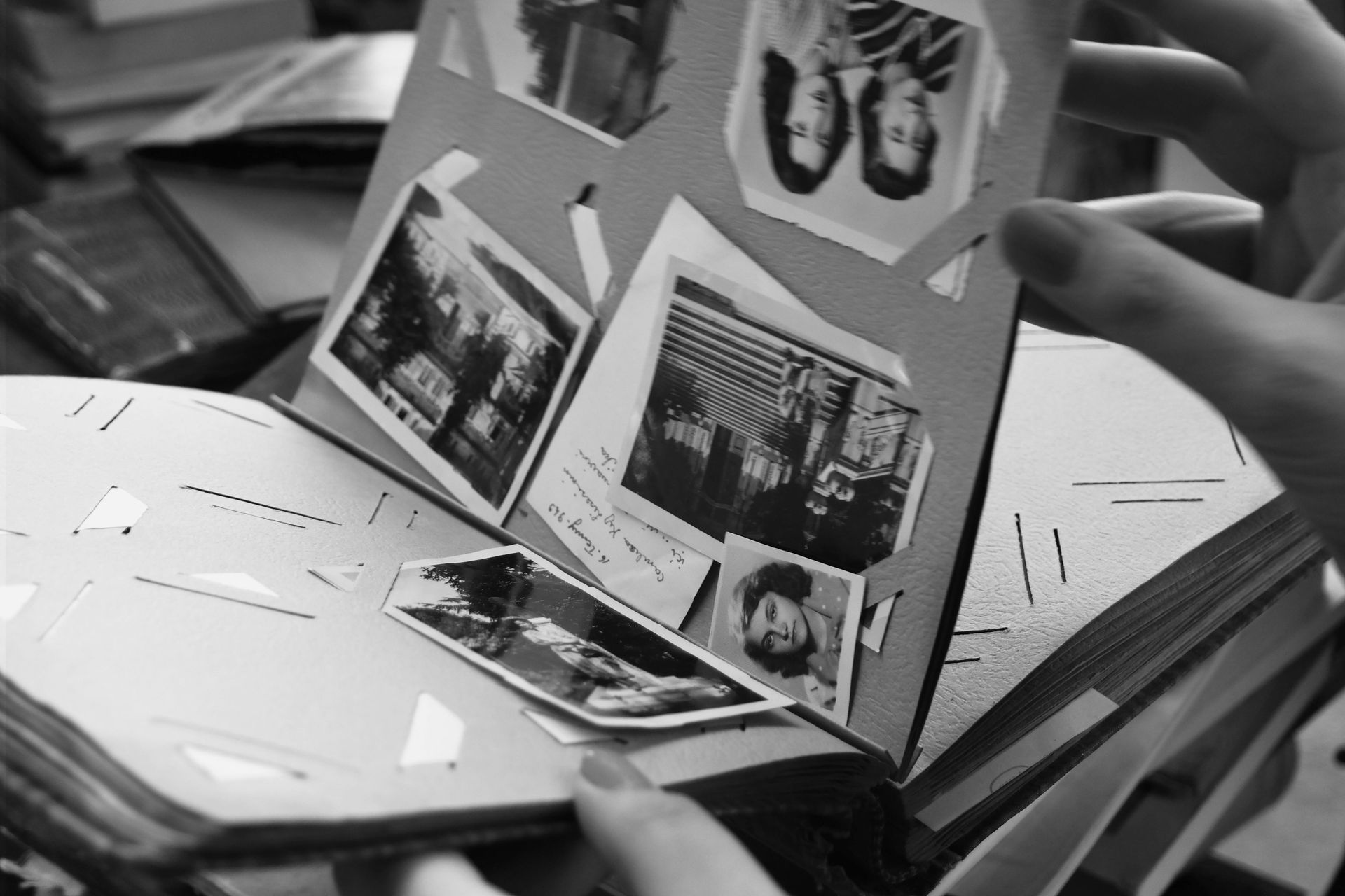 Hands flip through the pages of a black-and-white photo album filled with vintage photographs.