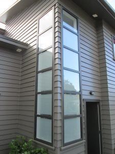 Corner of a building with tall windows and dark siding. A door is to the right of the windows.