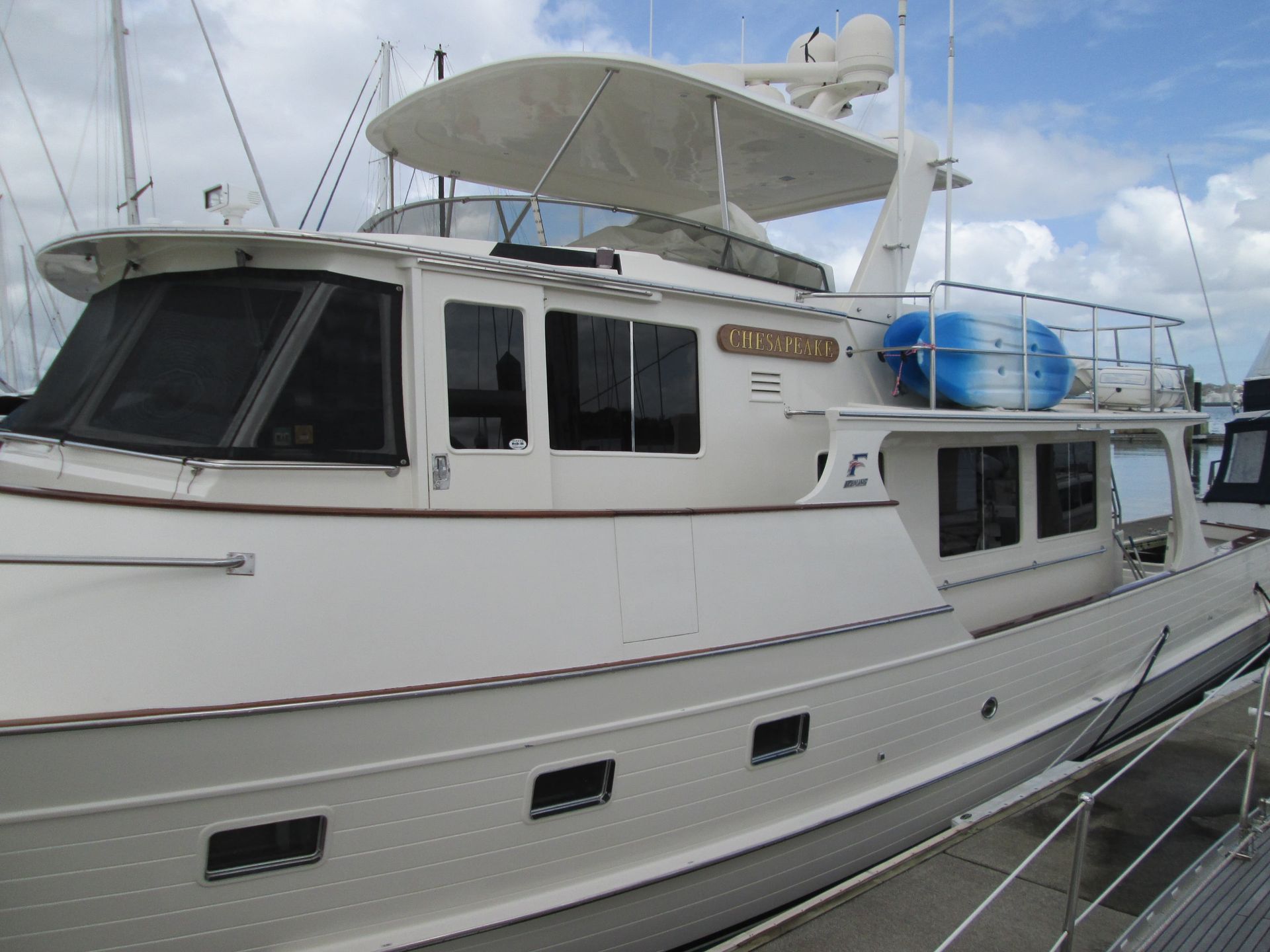 White yacht docked at a marina with windows, radar and life preserver, under a cloudy sky.