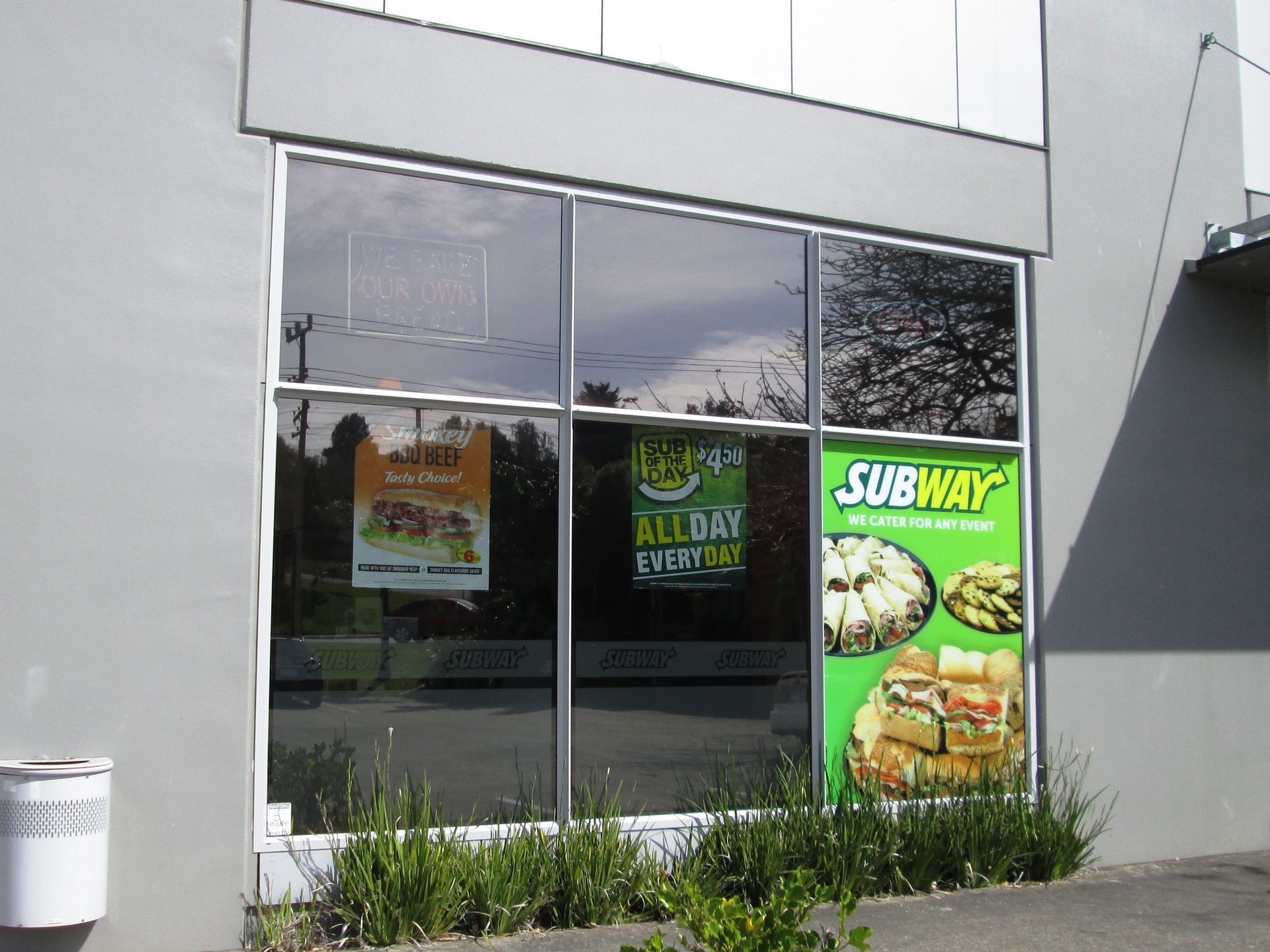 Subway restaurant storefront with window display, green and yellow sign, sandwiches shown.
