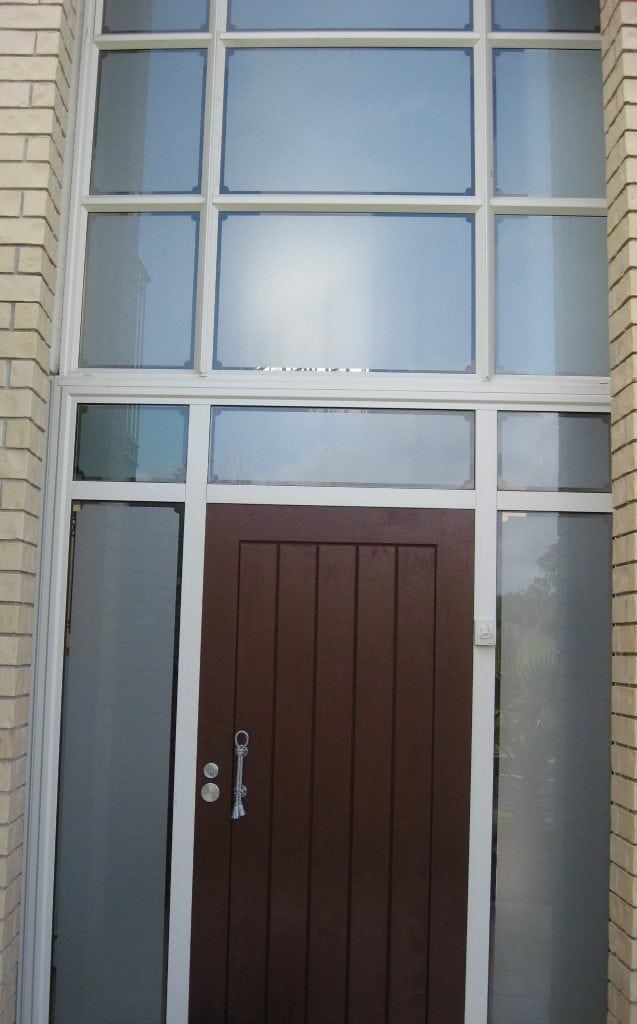 Brown door with sidelights and multi-pane transom, set in brick.