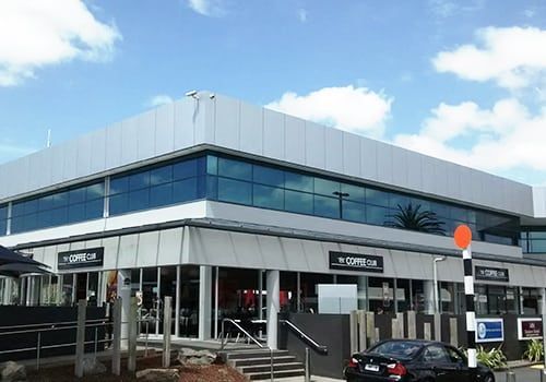 Modern commercial building with glass windows, cafe, and a black car.