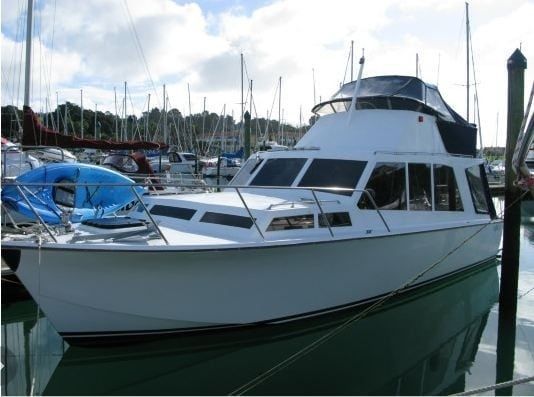 White motorboat in a marina, reflected in the water. Blue tarp is visible on the left side of the boat.