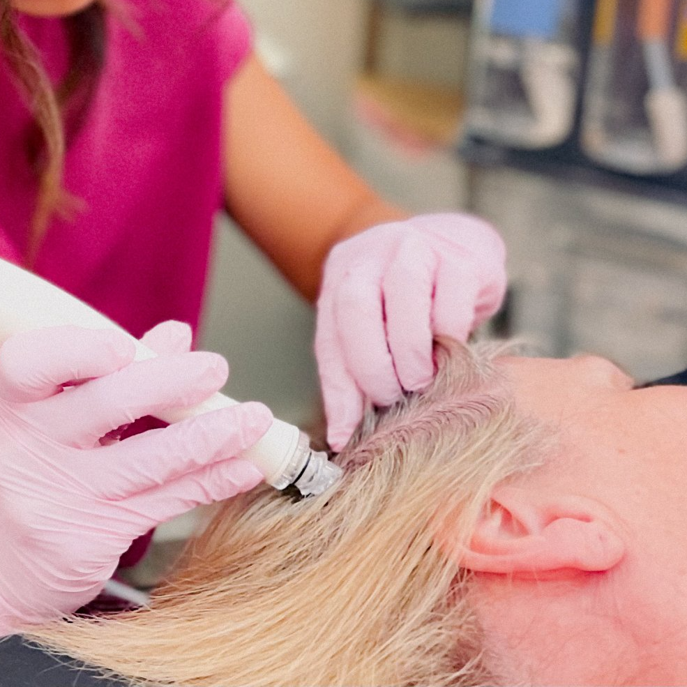 A woman wearing pink gloves is applying a cream to a woman 's hair