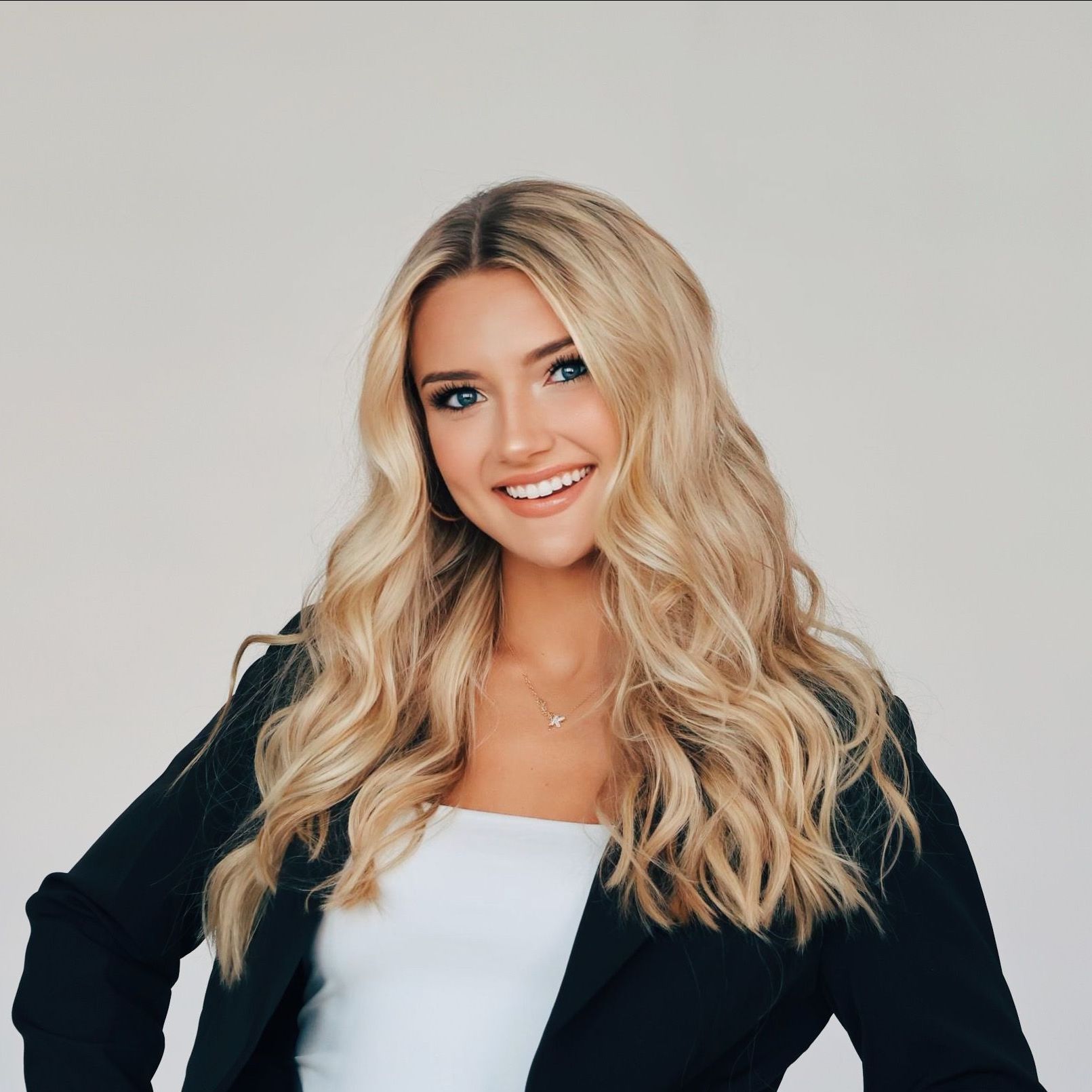 A woman with long blonde hair and blue eyes is wearing a tan jacket.