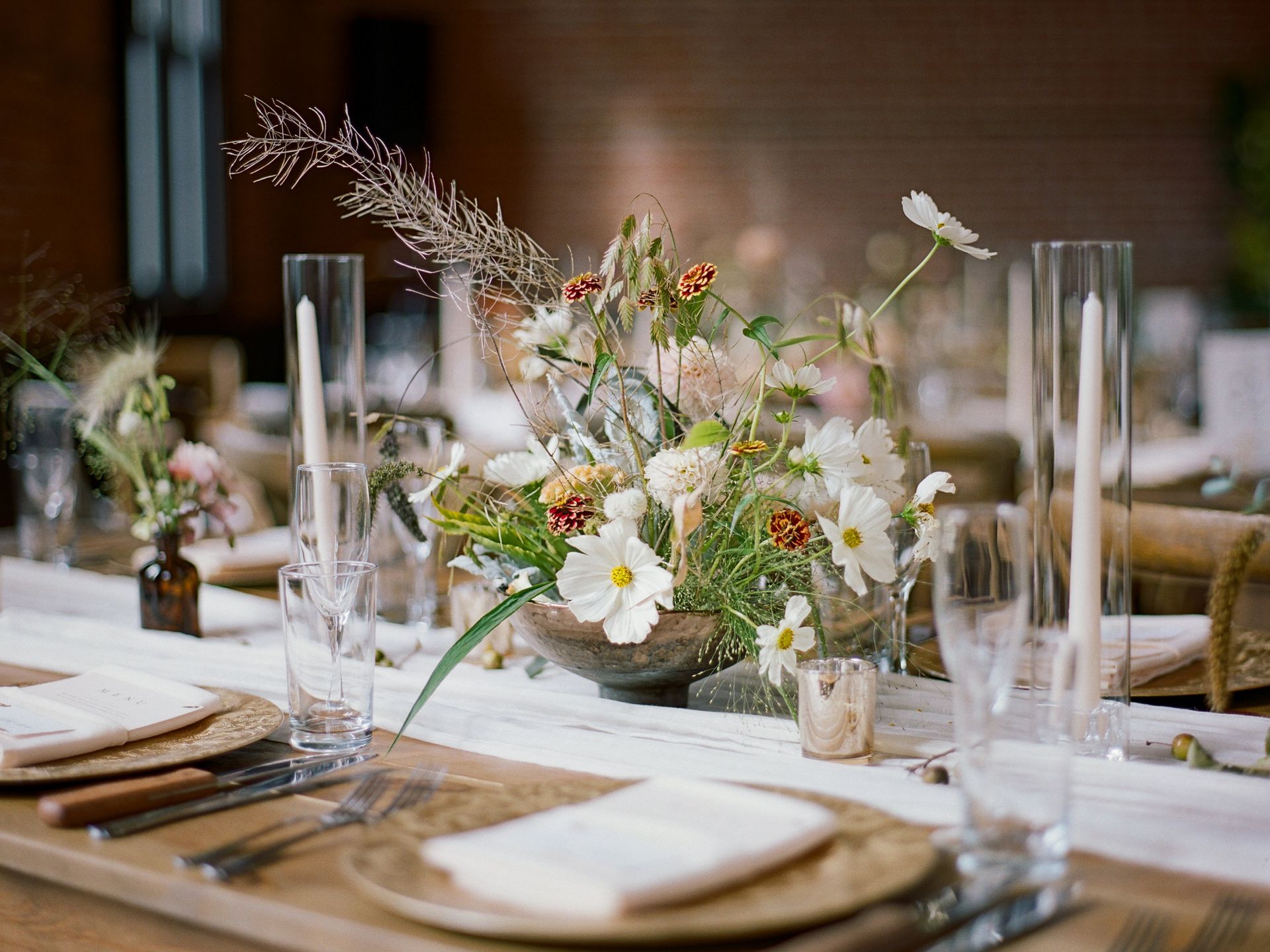 A long table with plates , glasses , and flowers on it.