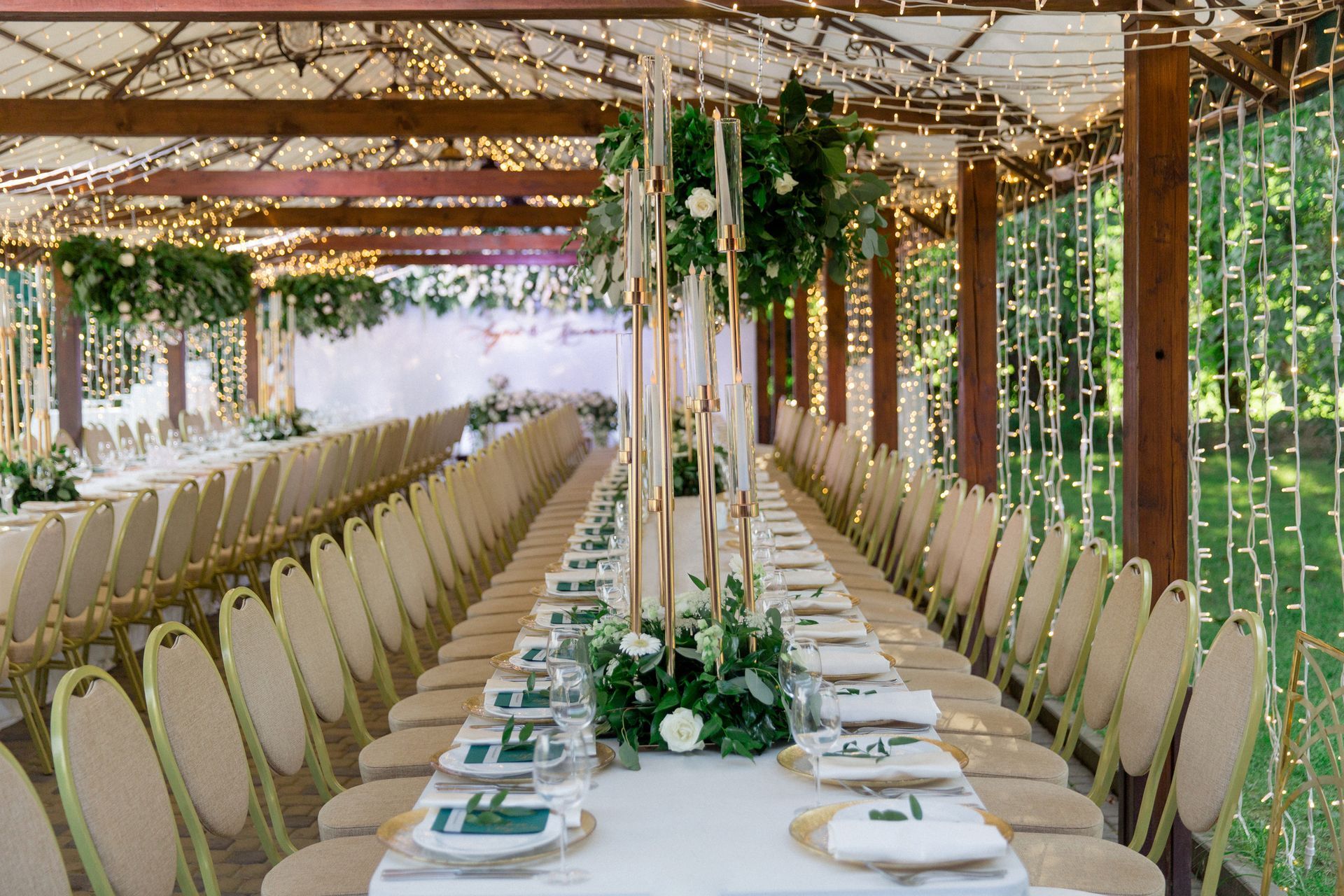 A long table with plates , napkins and candles is sitting under a canopy.