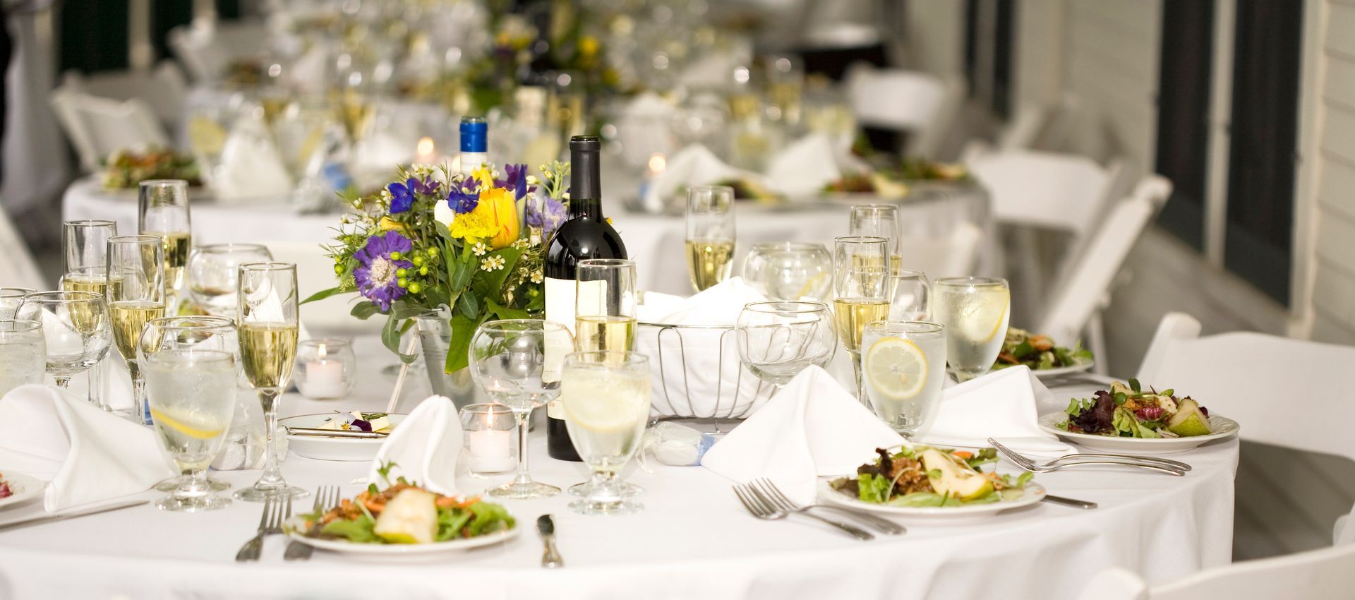 A table set for a wedding reception with plates of food and glasses of wine.