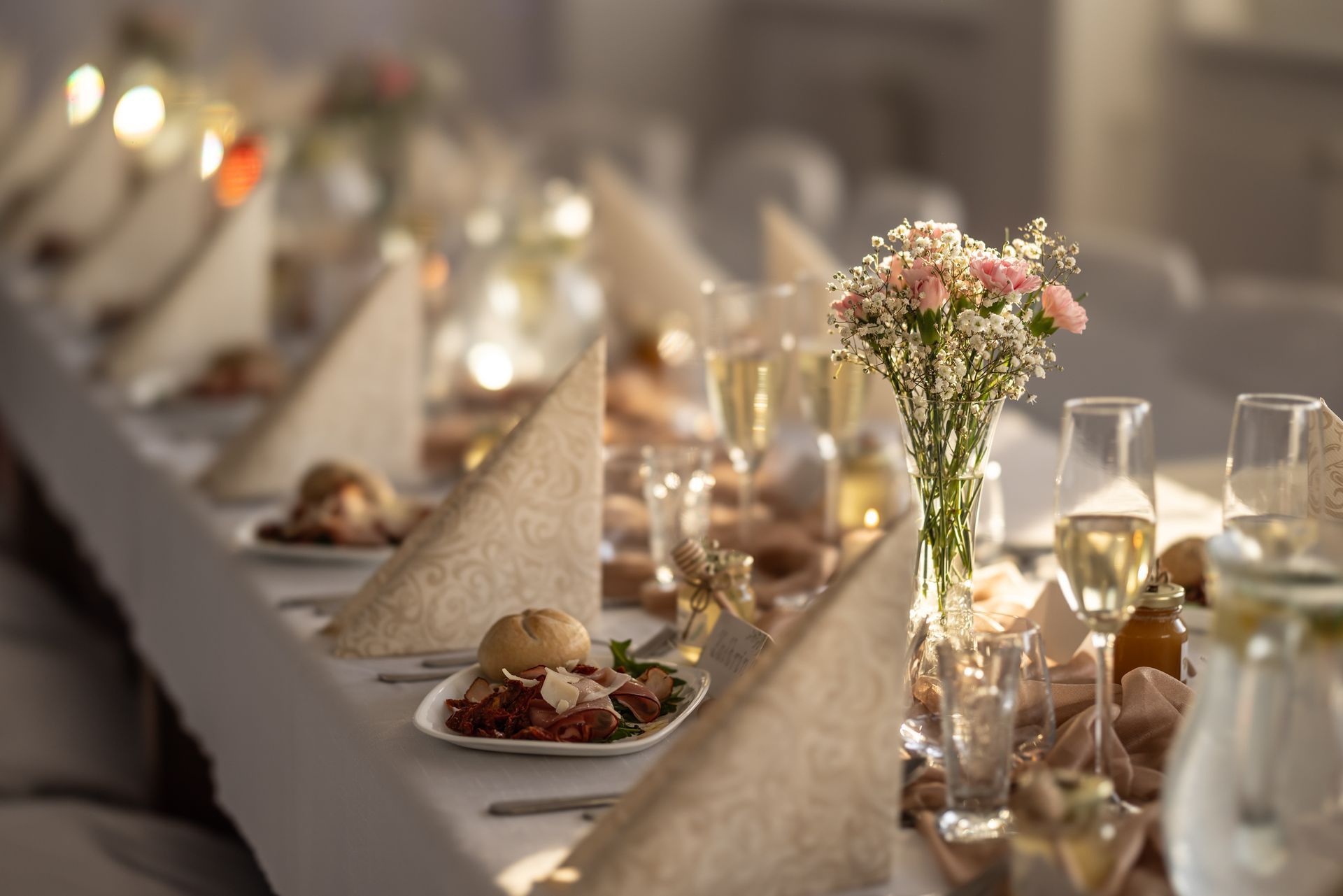 A long table set for a wedding reception with plates of food and glasses of wine.
