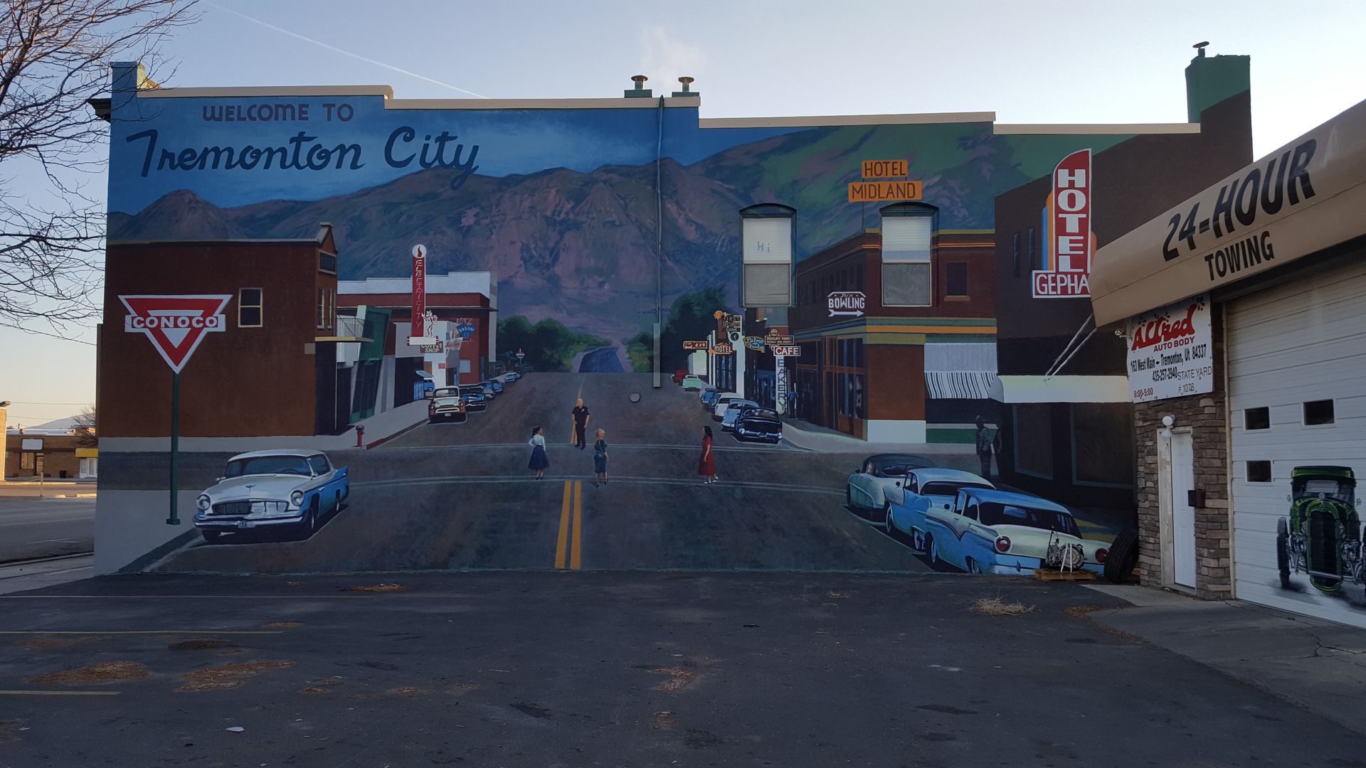 Mural of a town with cars, buildings, and a mountain in the background. A road in the foreground.