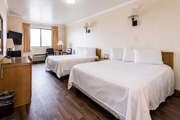 A motel room with two beds, a desk, a window, and wood-look flooring.