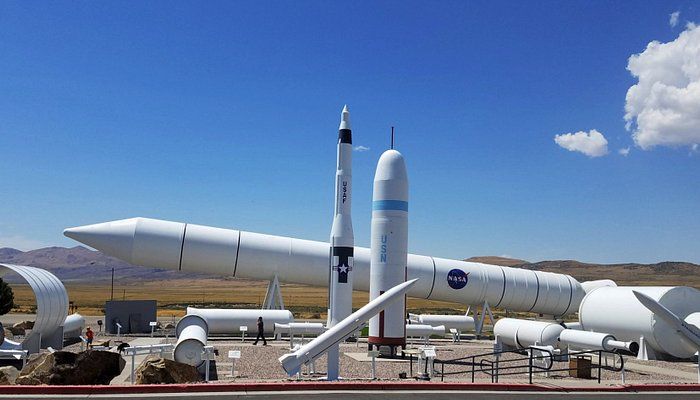 Collection of white rocket replicas outdoors against a blue sky, NASA logo visible.