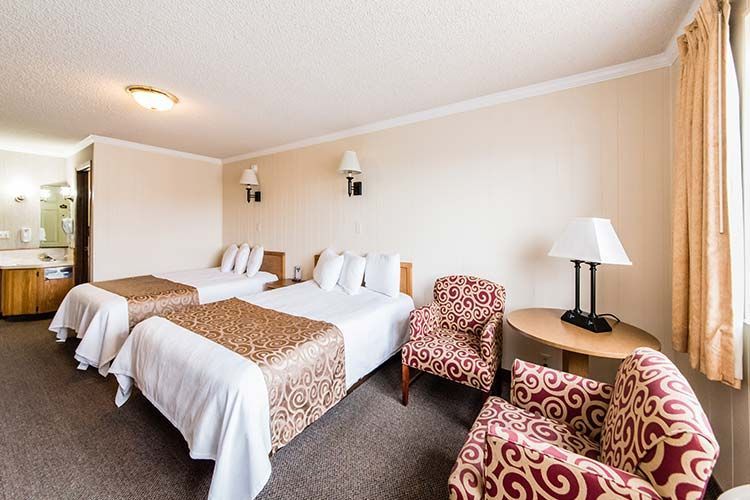 Hotel room with two beds, chairs, and a table near a window with curtains.