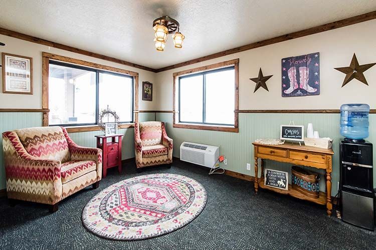 Waiting room with patterned armchairs, oval rug, small desk, and water cooler.