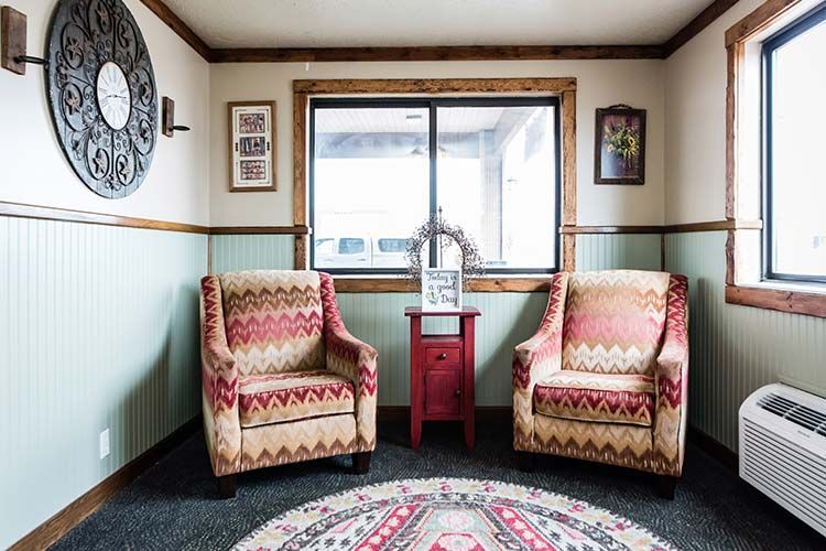 Cozy seating area with two patterned armchairs, small red side table, round rug, and a window.