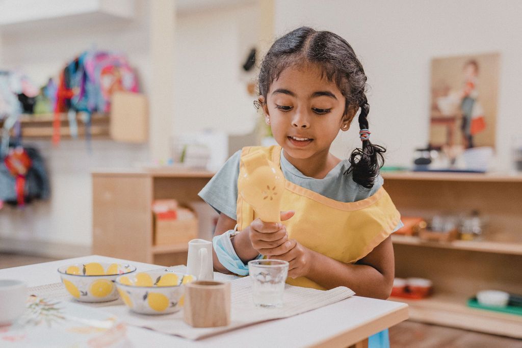 a little girl in a yellow apron sits at a table playing with lemons