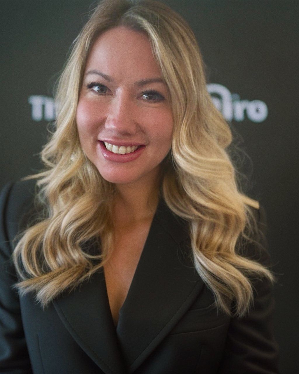 A woman with blonde hair and a black jacket is smiling