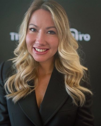A woman with blonde hair and a black jacket is smiling